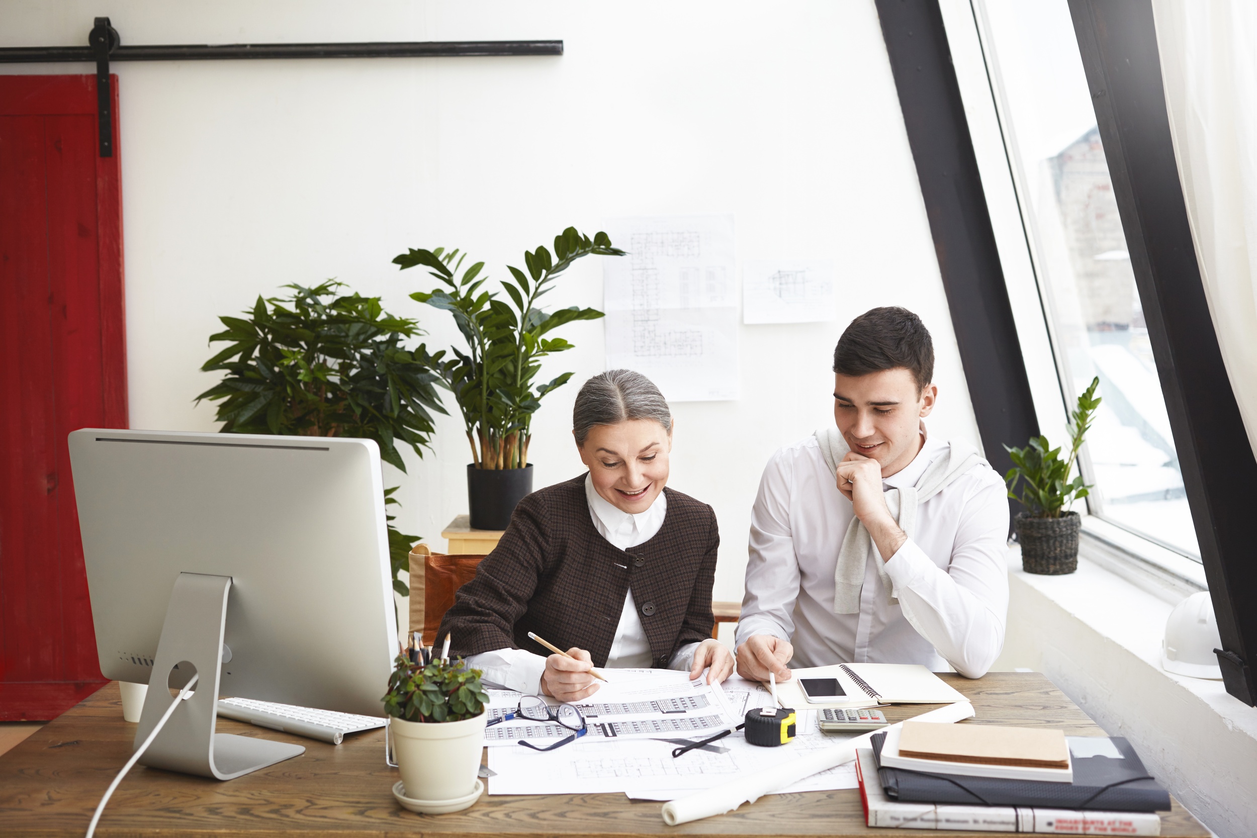 cheerful-elderly-female-chief-architect-young-male-working-together-architectural-project-happy-with-great-results-their-common-work-talking-smiling-teamwork-collaboration.jpg